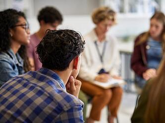 blurred photograph of a group of young people sitting around in a focus group/discussion setting with someone taking notes